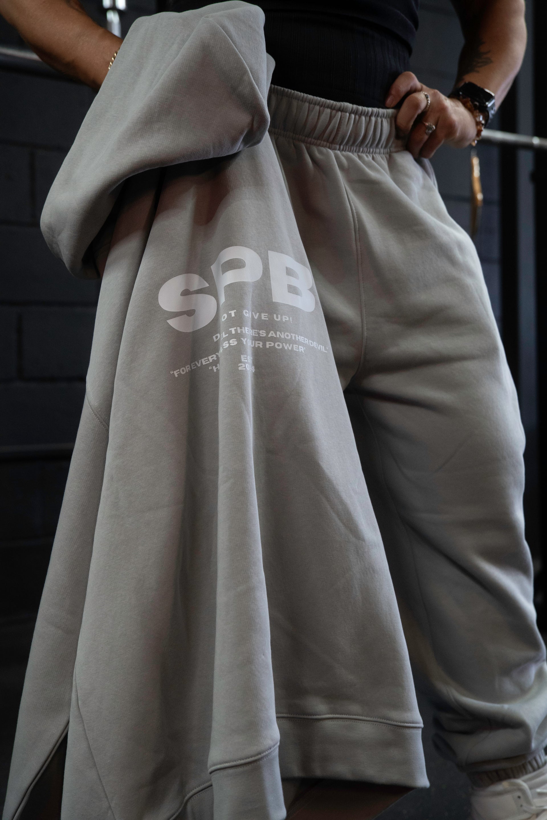 Person wearing gray SPB bottoms and holding gray SPB hoodie.