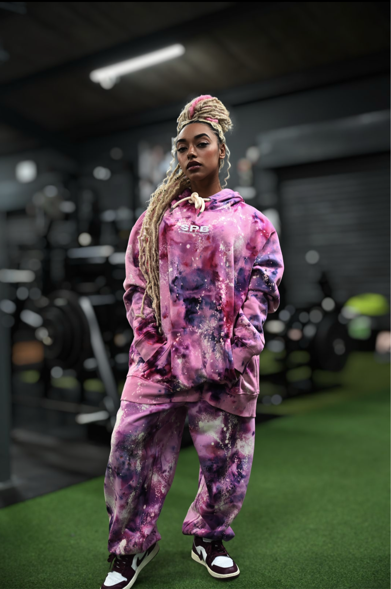 Person wearing a pink tie-dye SPB outfit standing on a green surface in a gym setting.