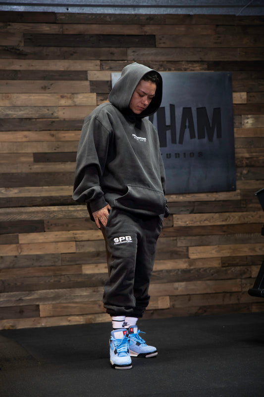 Person wearing SPB hoodie and bottoms in front of a wooden panel wall backdrop.