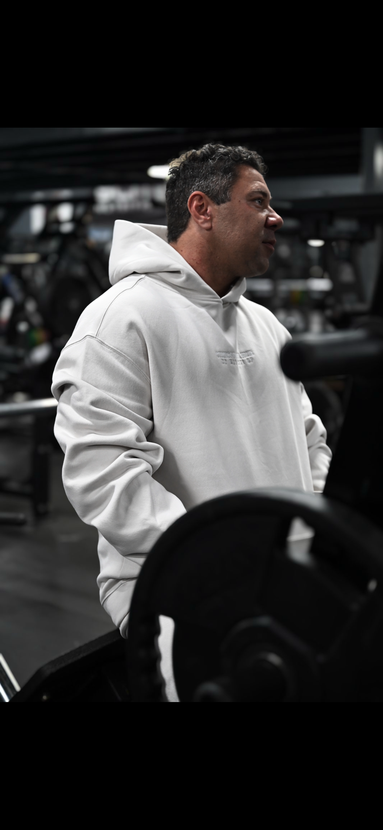 Man in a white SPB hoodie standing in a gym setting.