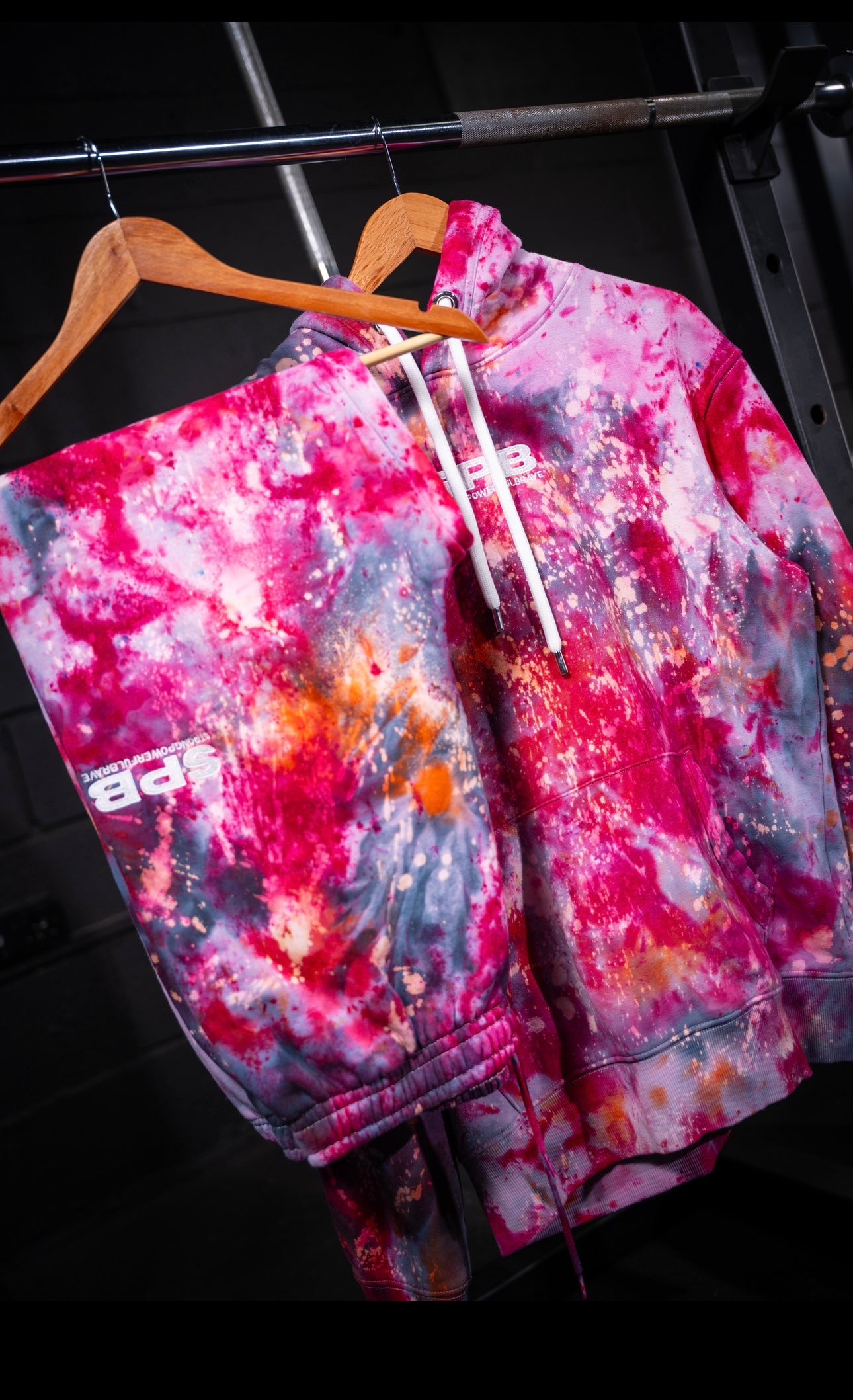Pink rain branded  tie-dye set with a brand logo on a hanger against a dark background