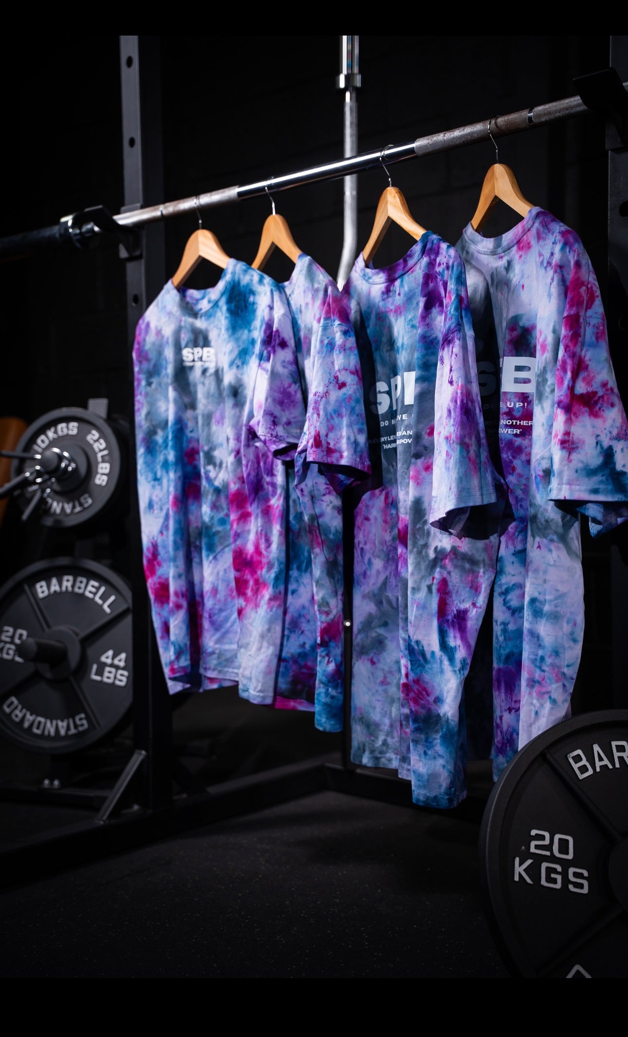 Colorful tie-dye outfits hanging on a rack with gym equipment in the background