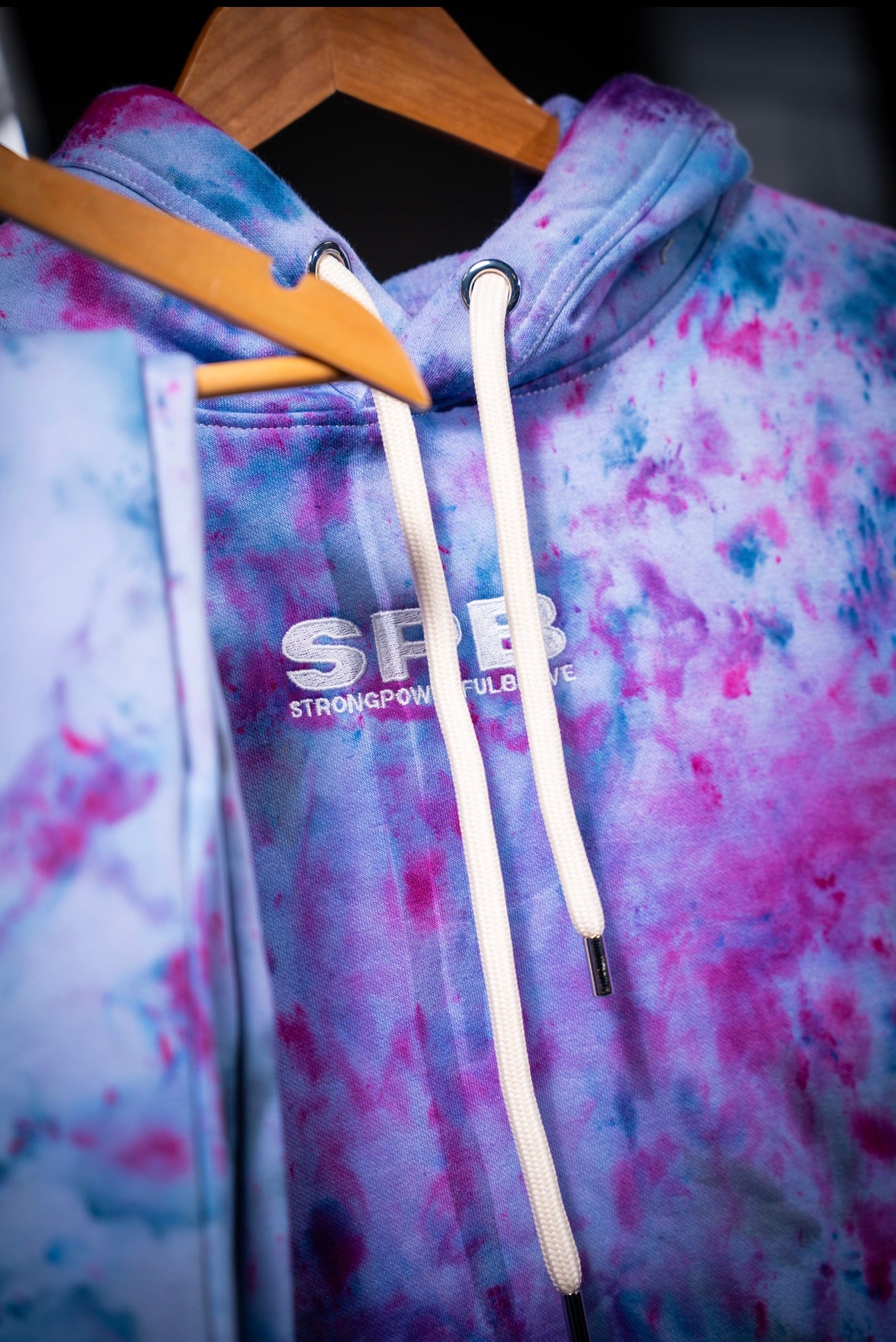 Purple rain tie-dye hoodie with a visible brand logo on a hanger.