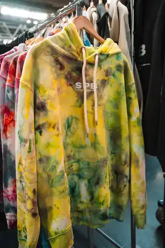 Yellow/Green tie-dye hoodie with 'SPB' branding on a rack of clothes.
